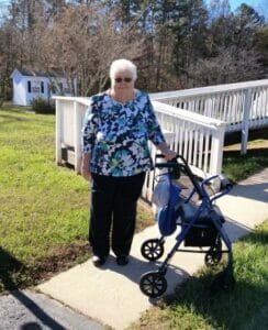 A woman, Nancy Harlow, with a walker stands near an ADA accessible ramp.